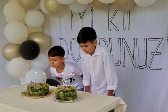 Two boys joyfully blow out candles on cakes at a birthday celebration with balloons.
