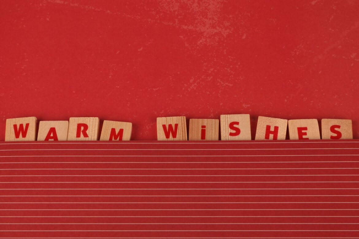Wooden scrabble tiles spelling 'Warm Wishes' on a festive red background.