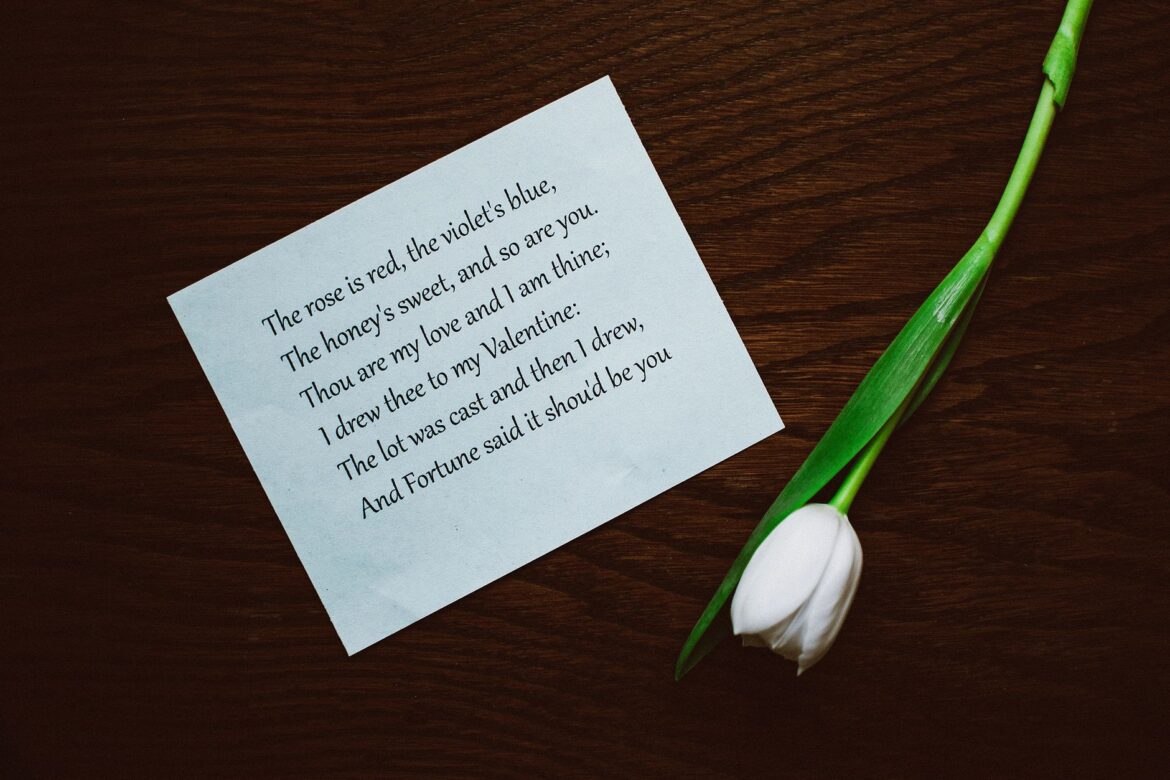 A Valentine's Day poem beside a white tulip on a dark wooden table, evoking romance.