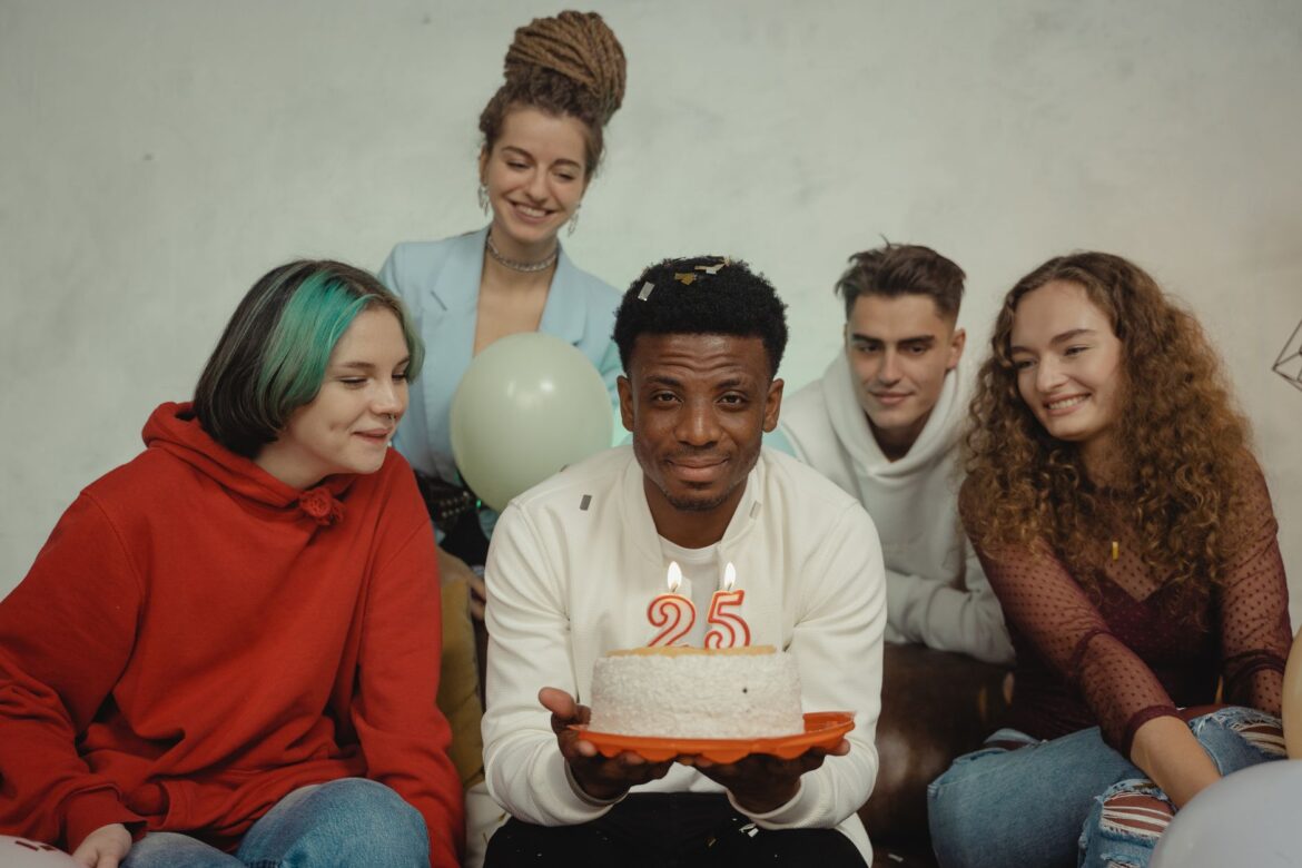 A joyful group of friends celebrating a 25th birthday indoors with a cake and candles.