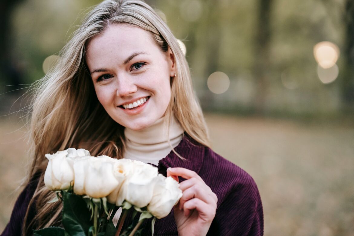 Happy young female in casual wear with long hair with bunch of white roses looking at camera smiling