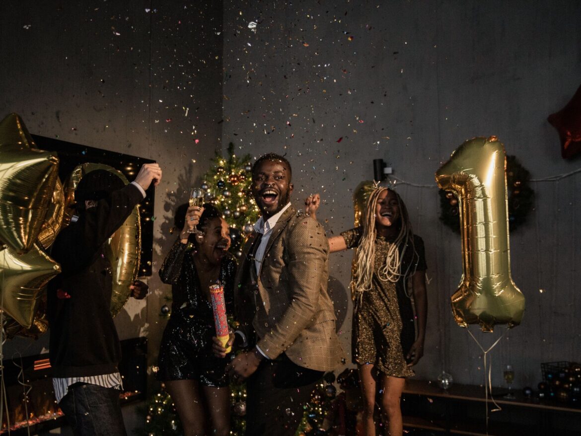 Group of friends celebrating New Year indoors with confetti and balloons, radiating joy and happiness.