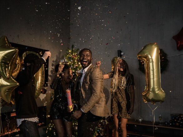 Group of friends celebrating New Year indoors with confetti and balloons, radiating joy and happiness.