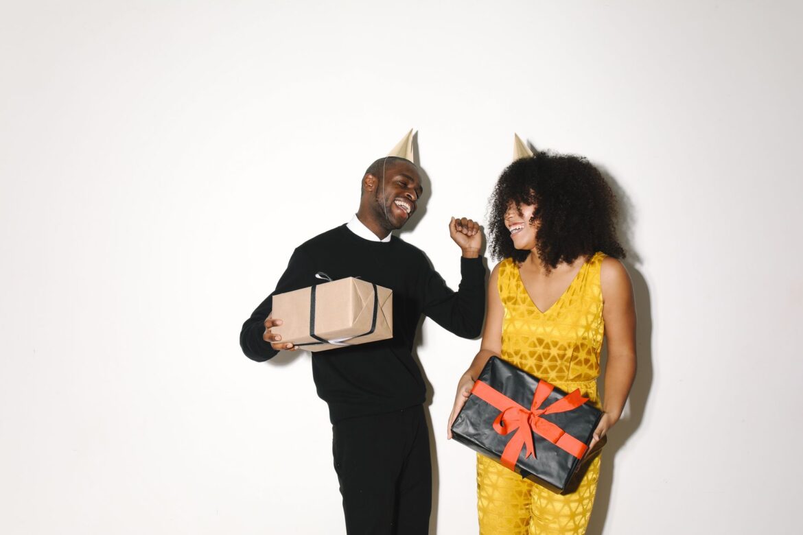 A cheerful couple wearing party hats, holding gift boxes and smiling, perfect for festive celebrations.