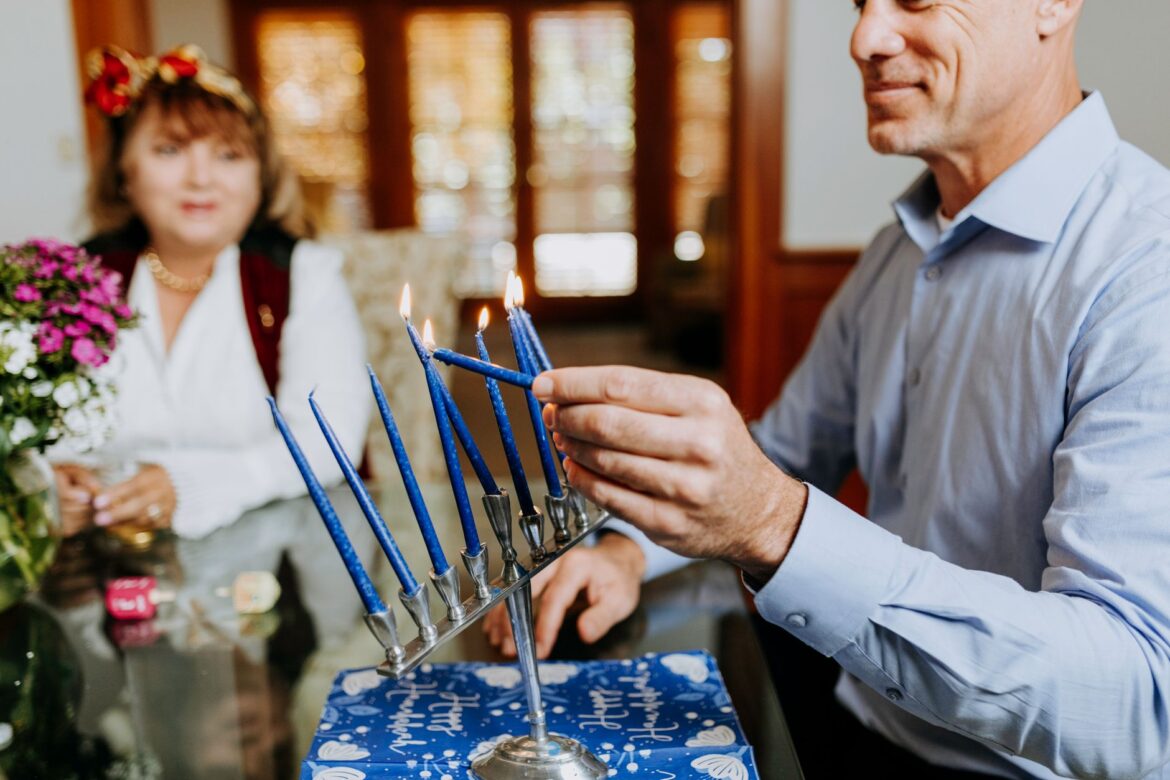 A family gathers indoors to celebrate Hanukkah by lighting the menorah candles. Warm and festive atmosphere.