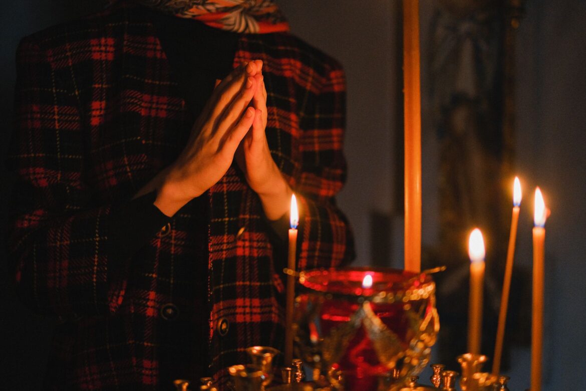 A person praying with candles in a dark, spiritual church setting.