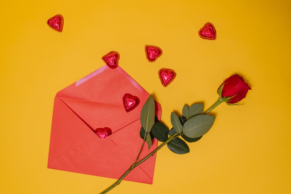 A romantic setup with a red rose and heart-shaped chocolates on a yellow background.