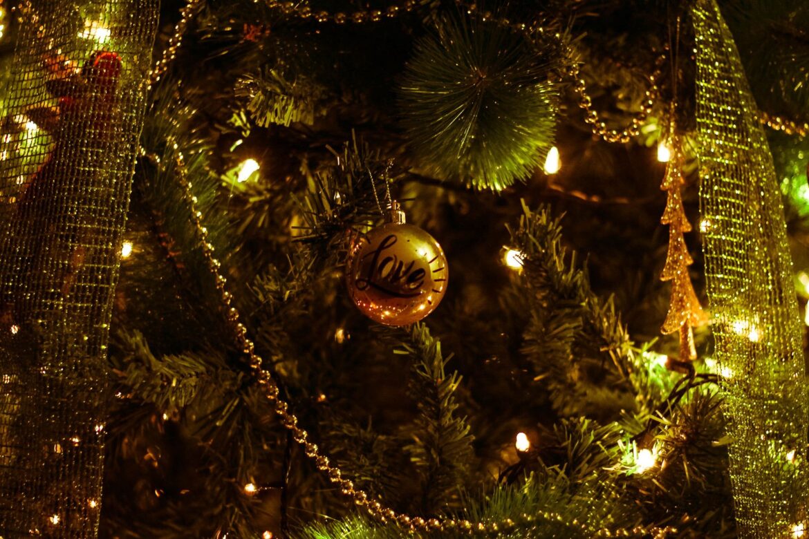 Glistening gold ornament with 'Love' on a lit Christmas tree, creating a warm holiday atmosphere.