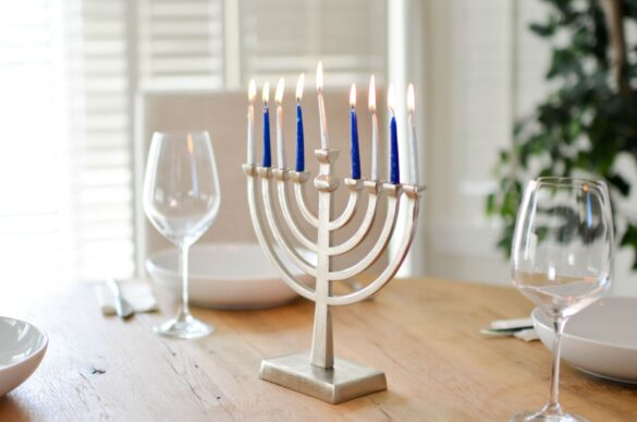 A beautifully set table for Hanukkah with a lit menorah and elegant tableware.