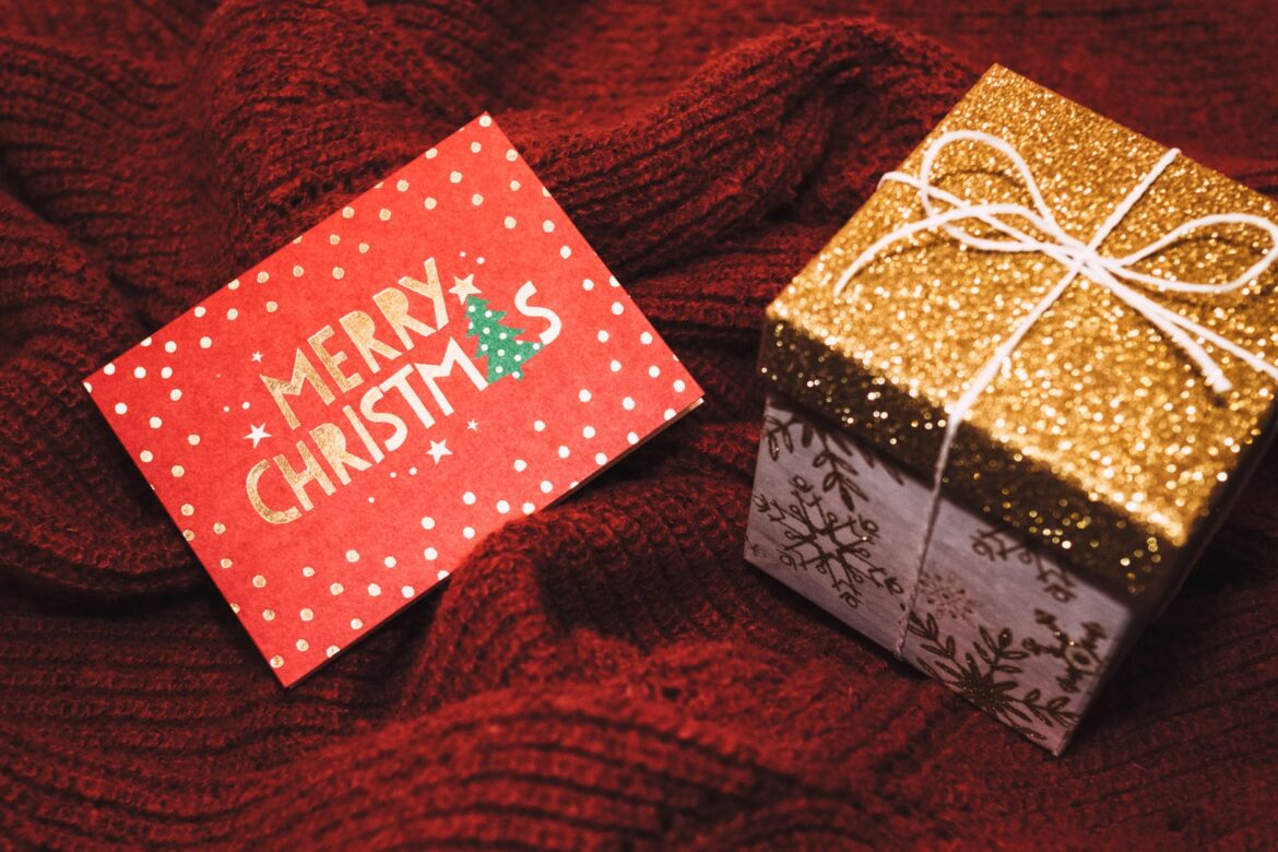 A joyful scene with a 'Merry Christmas' card and a glittery gift box on red fabric.