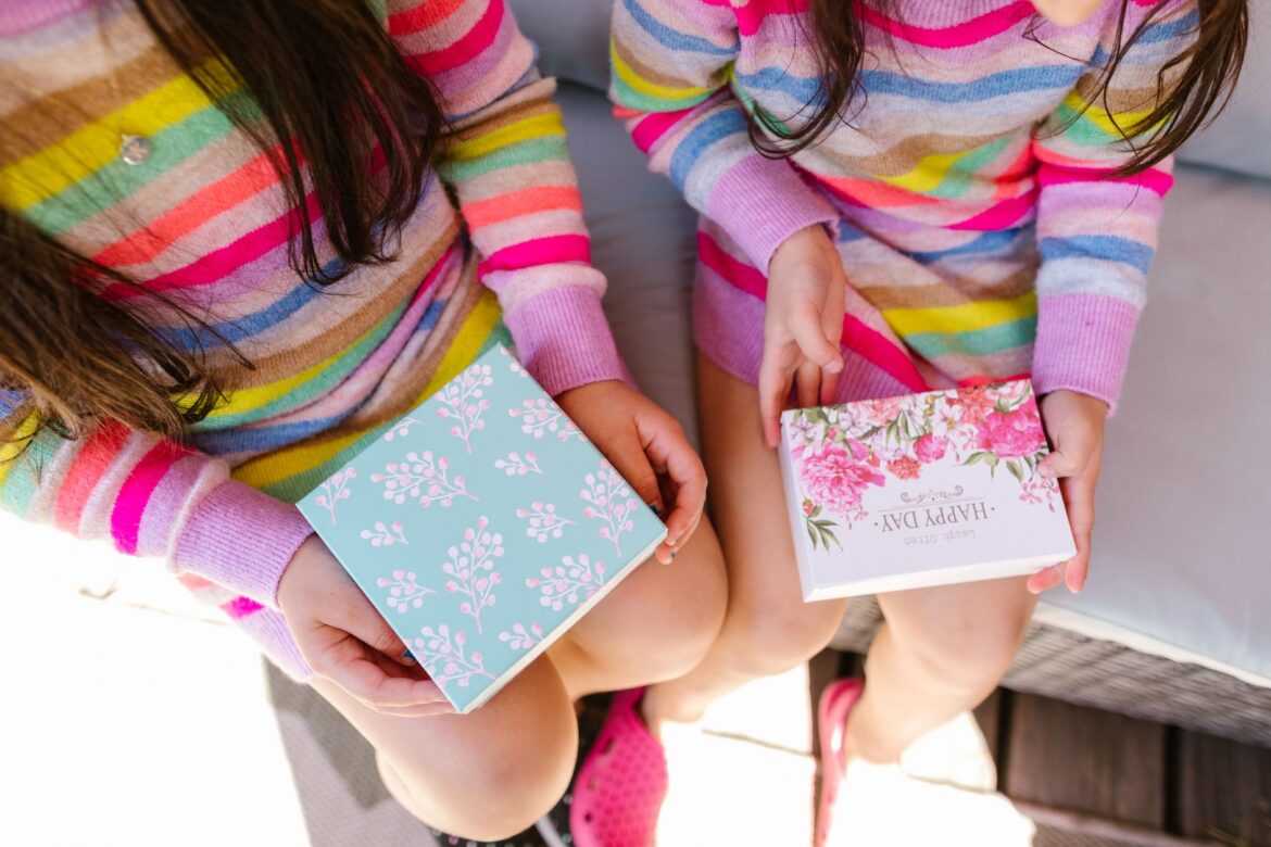 Two children in striped sweaters hold decorative gift boxes. Bright and joyful scene.