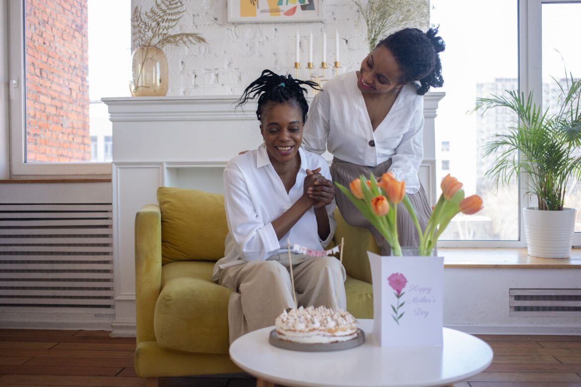 A joyful Mother's Day moment with mother and daughter, cake, and tulips indoors.