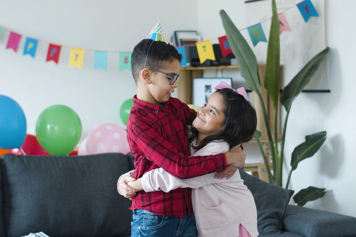 Two cheerful children embrace at a lively birthday party with colorful decorations indoors.