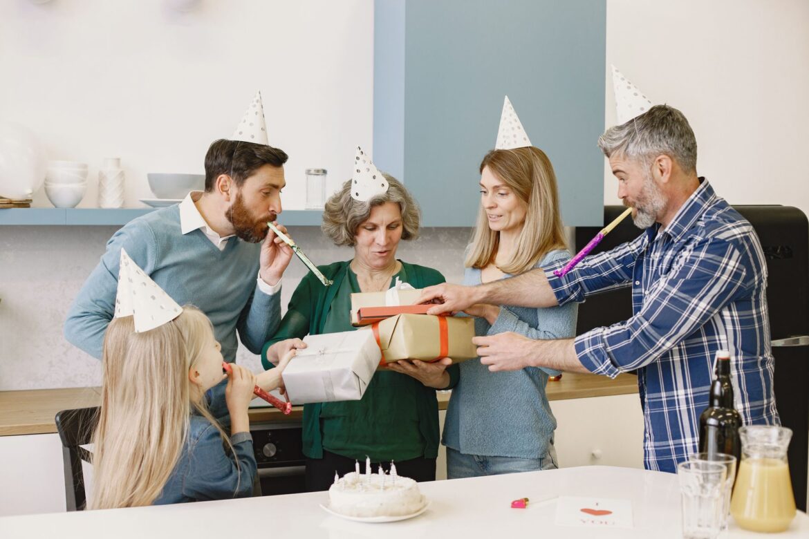 Happy family celebrating with party hats, gifts, and a cake indoors.