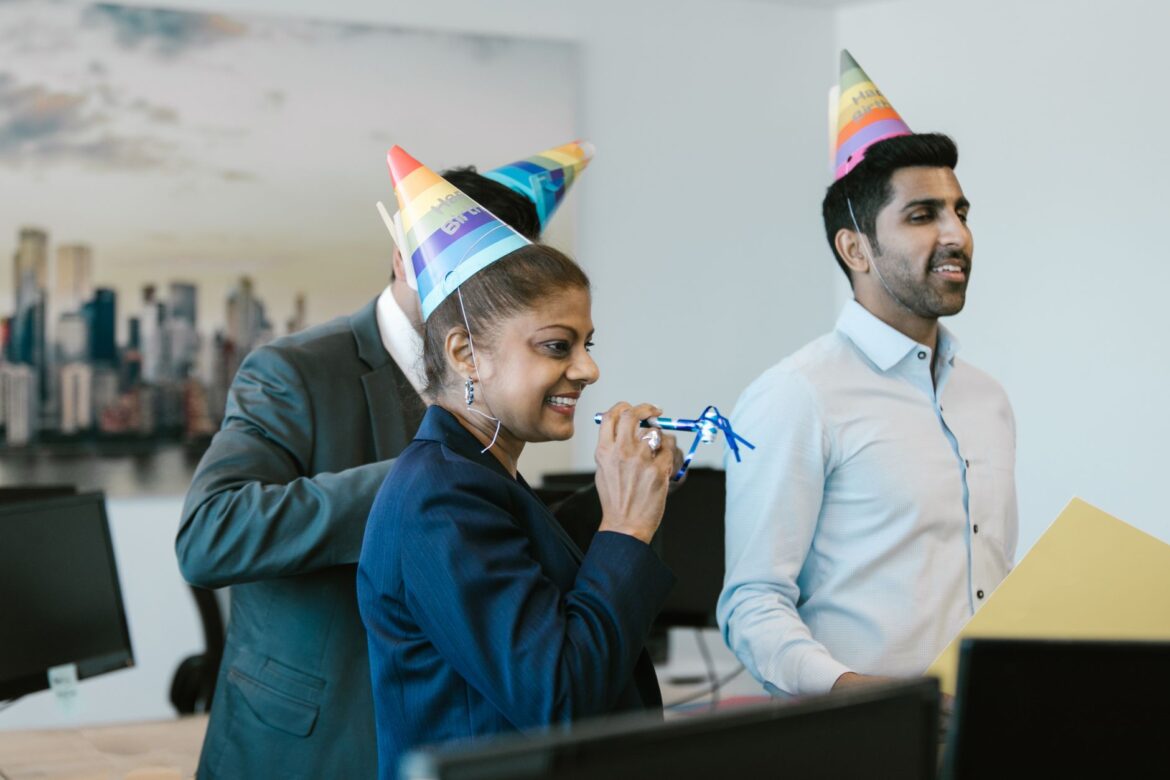 Colleagues celebrating a birthday in the office with colorful hats and smiles.