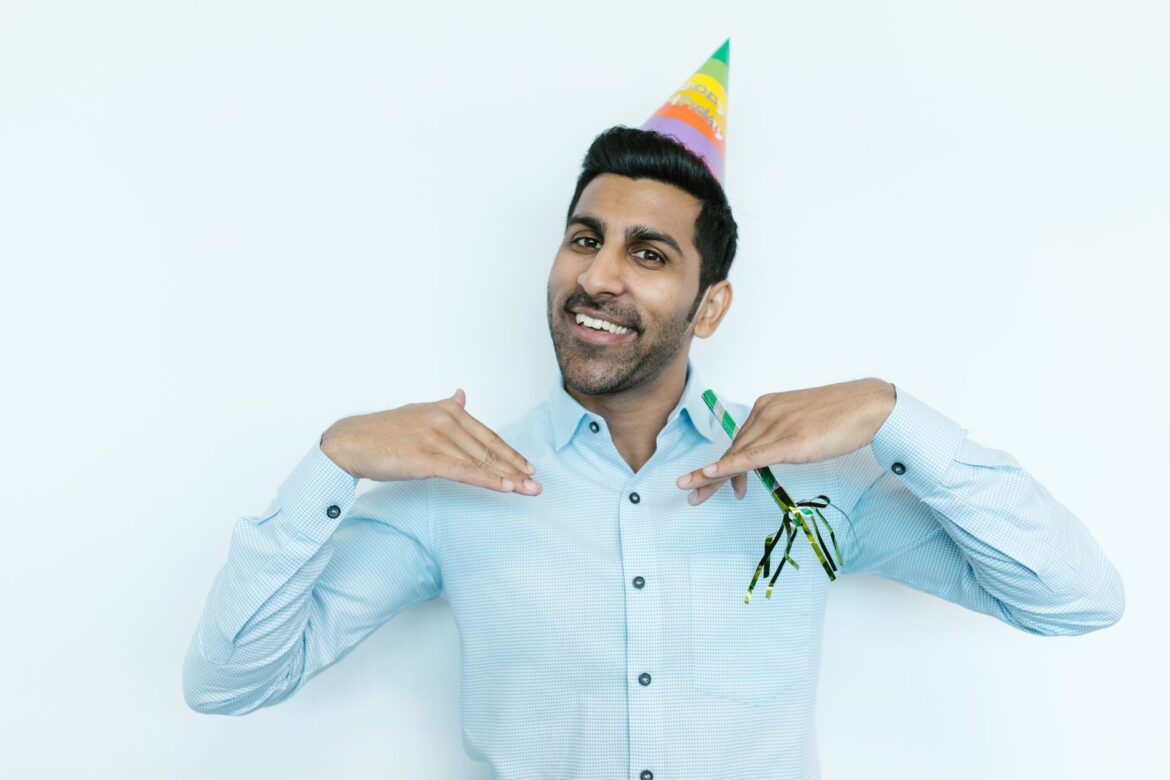 Cheerful man in a festive party hat celebrating in an office environment. Ideal for business and celebration themes.
