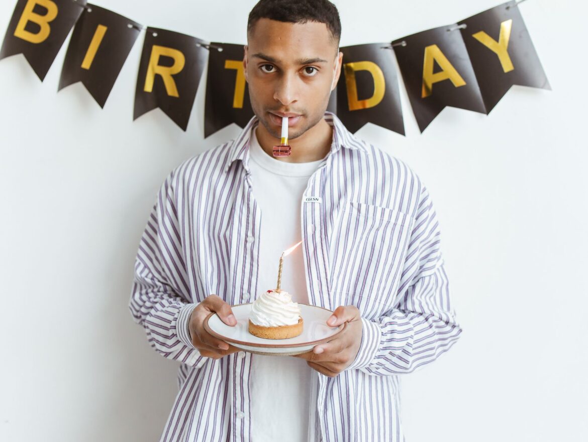 Young man celebrating birthday with a cupcake and candle indoors.