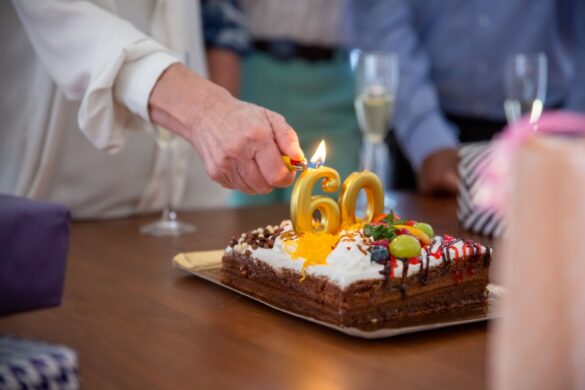Hand lighting candles on birthday cake with number 60 on it at a celebration.
