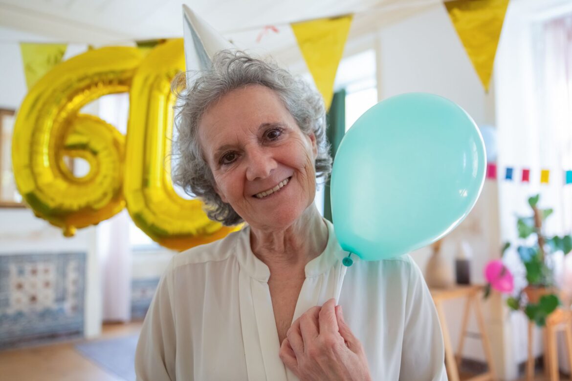 Elderly woman cheerfully celebrating her 60th birthday indoors with balloons.