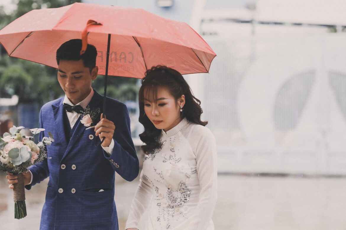 A charming couple walking in the rain during their wedding, sharing an umbrella.