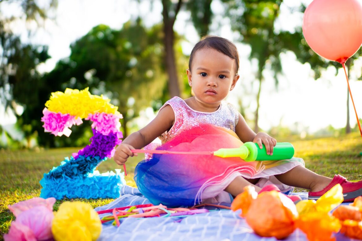 Adorable toddler enjoying a colorful outdoor birthday party with balloons and decorations.