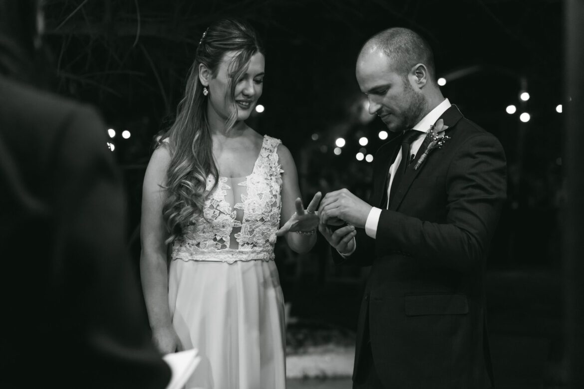 A candid moment of a couple exchanging rings during their outdoor wedding ceremony at night.