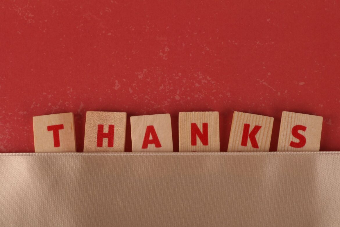 Wooden tiles with red letters spell 'Thanks', set against a red backdrop with a beige strip.