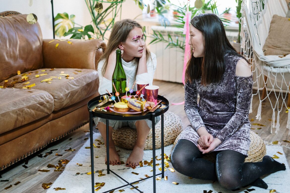 Two friends having a lively indoor celebration with confetti and decorations around them.